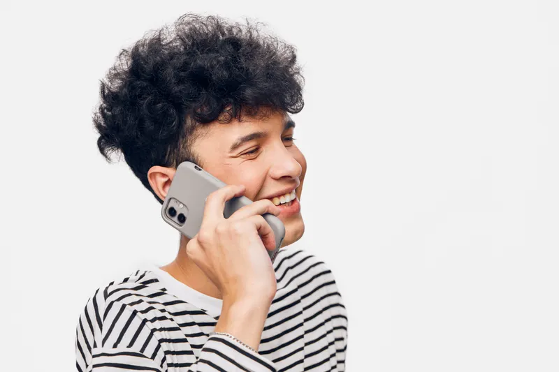 young man talking on smartphone smiling, wearing striped shirt, curly hair, positive mood, isolated white background, casual communication scene