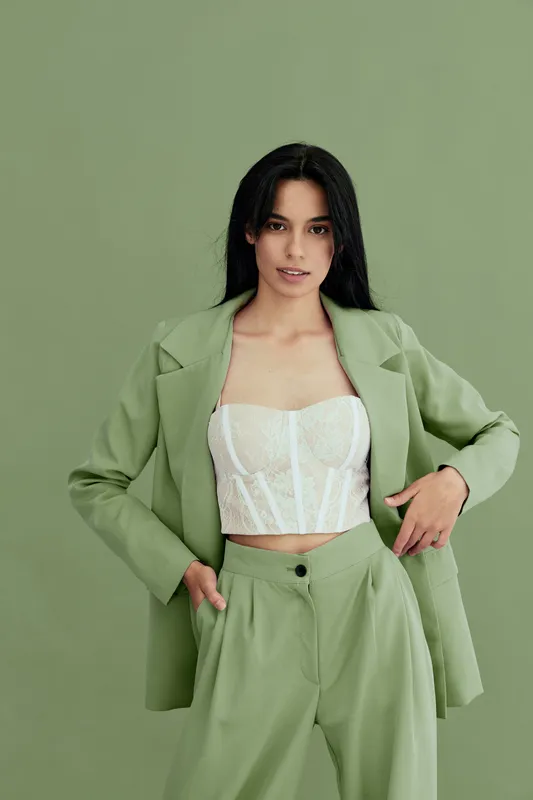 young woman wearing pastel green suit and white corset top, posing confidently against matching green backdrop in stylish modern fashion portrait