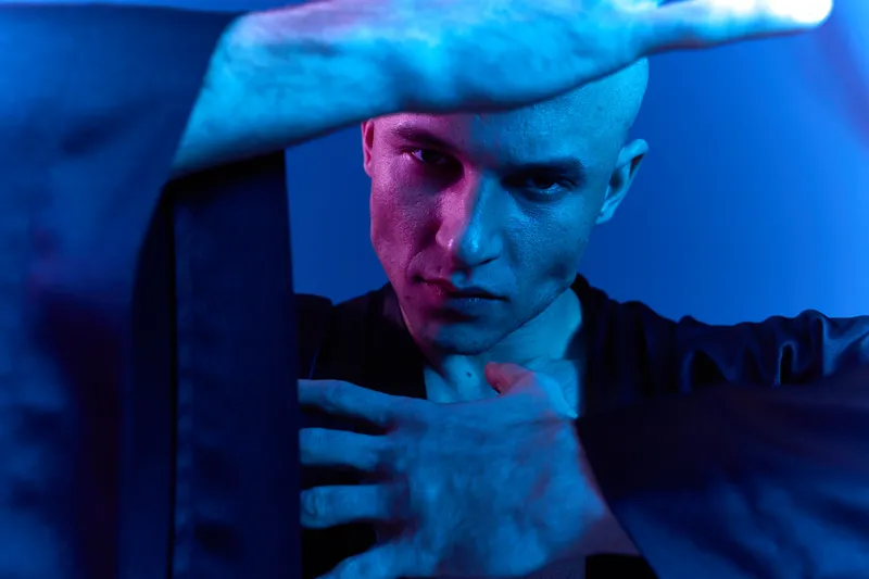 Intense man with a dramatic expression, showcasing strength and determination, set against a vibrant blue background. The image captures a vivid moment of focus and energy.