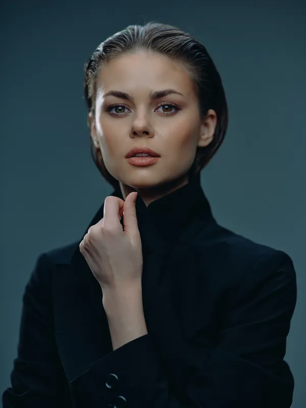 Elegant woman with wet hair wearing a black coat, posing confidently with a dark background and soft lighting.