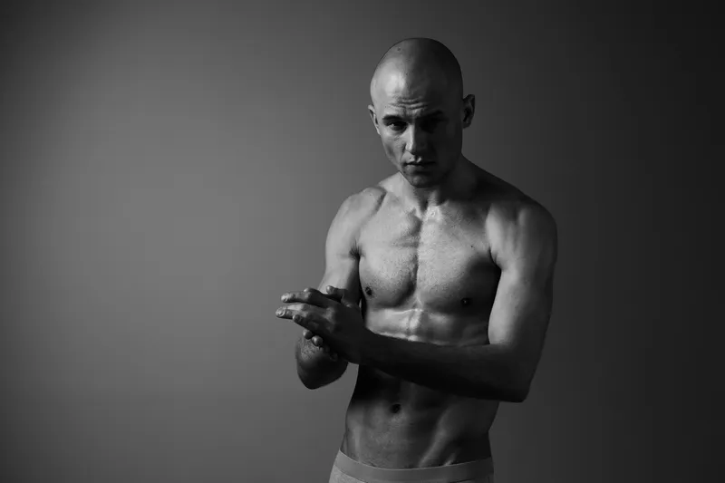 Strong man preparing for training, showcasing determination and focus in a black and white image that emphasizes muscular definition and intensity.