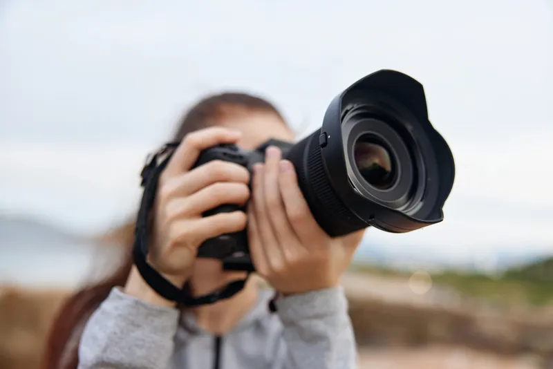 Young woman holding a professional camera outdoors, focusing on photography with nature background, showcasing passion for photography and creativity