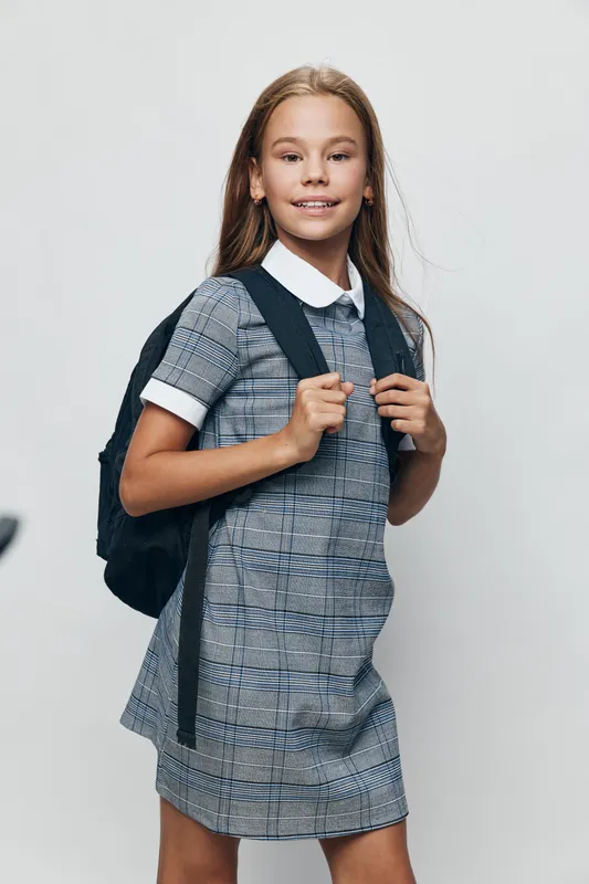 Girl with backpack standing isolated on white background wearing school uniform, smiling and ready for education or study, childhood and student concept.