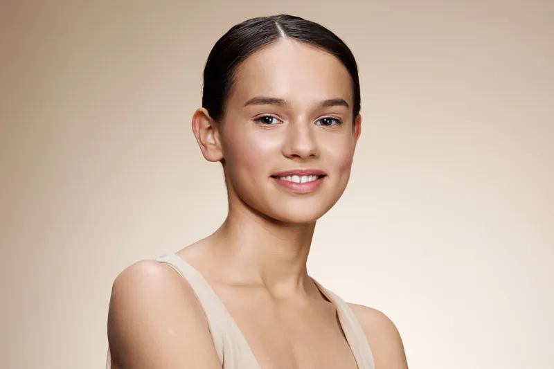 Natural portrait of a female model with a radiant smile and minimal makeup, showcasing healthy skin and a neutral background Perfect for beauty and skincare concepts