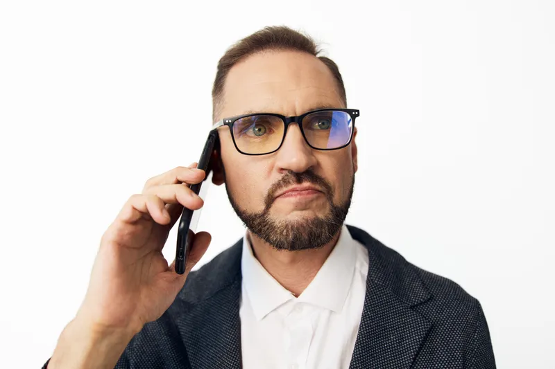 A professional man speaks on a mobile phone, set against an isolated color background. The scene conveys focus, determination, and seriousness, ideal for business and leadership themes.