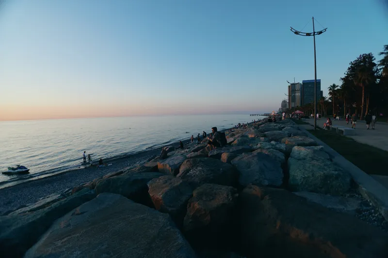 lifestyle woman in modern boho-western denim street style standing by rocky beach during sunset with film color tones
