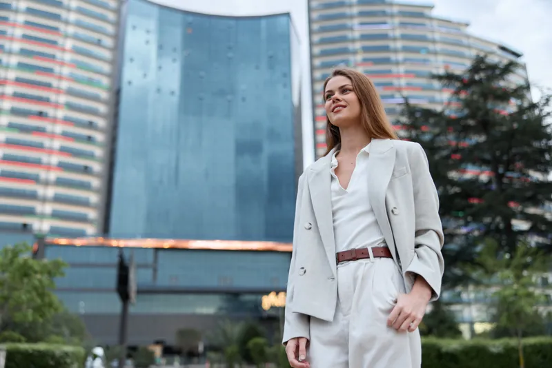 confident woman in business attire standing outdoors near modern skyscraper with urban background and professional expression