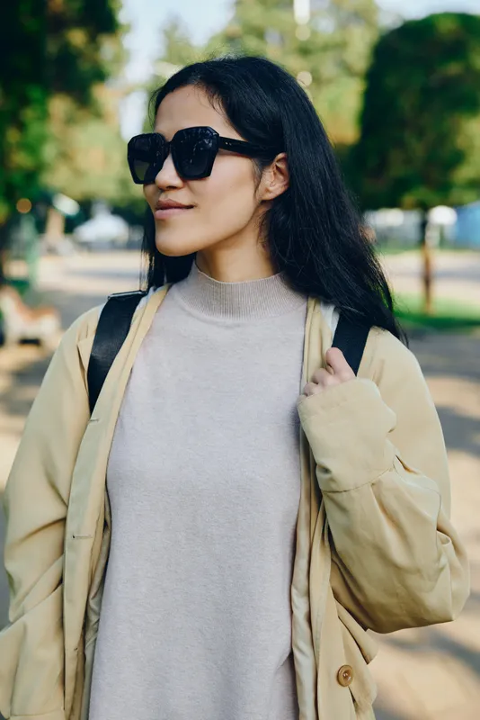 Woman sunglasses coat sweater outdoor fashion model style urban lifestyle, wearing beige outerwear and a cozy knit, in a sunny park backdrop with a casual, confident vibe.