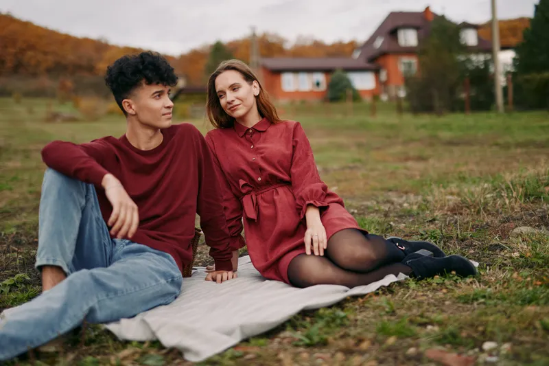 Young couple sitting on a blanket in a rural field, sharing a candid intimate moment that conveys authenticity and credibility through natural expressions, relaxed poses and simple autumn clothing.