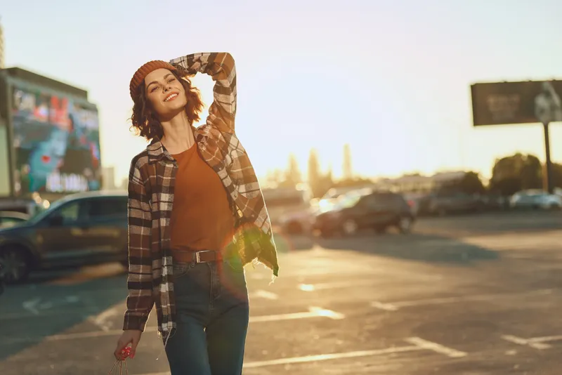 Woman smile golden hour urban candid lifestyle authenticity portrait in a parking lot, carefree joyful moment with warm sunset glow. Emotional storytelling and mindful living vibe in city light.