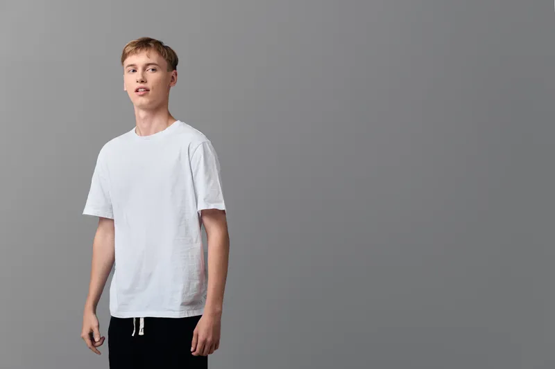Young man in a white t shirt stands in a studio, casual wear and relaxed pose against a gray background, a clean lifestyle image for fashion and product stock