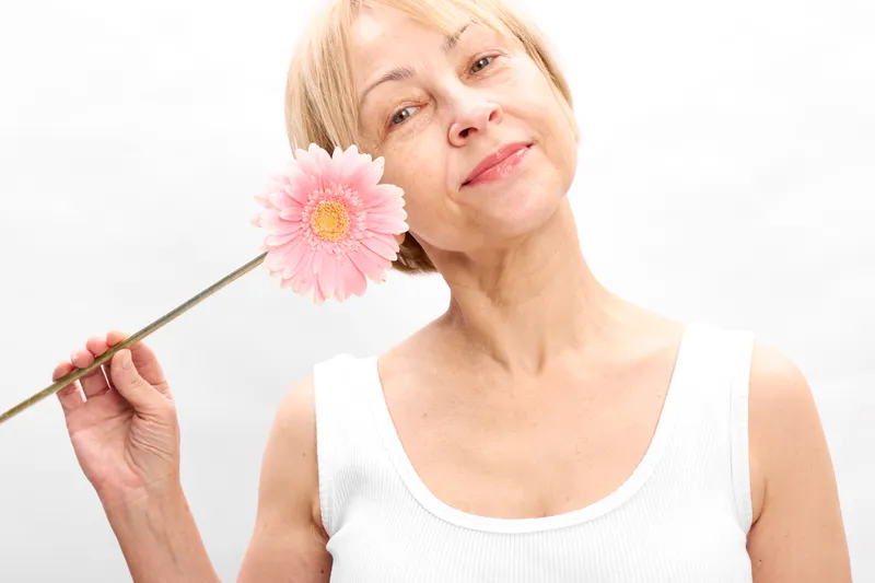 Woman holding pink flower, smile in soft studio light, close portrait against white background, spring freshness and beauty concept, gentle self care mood, nature elegance