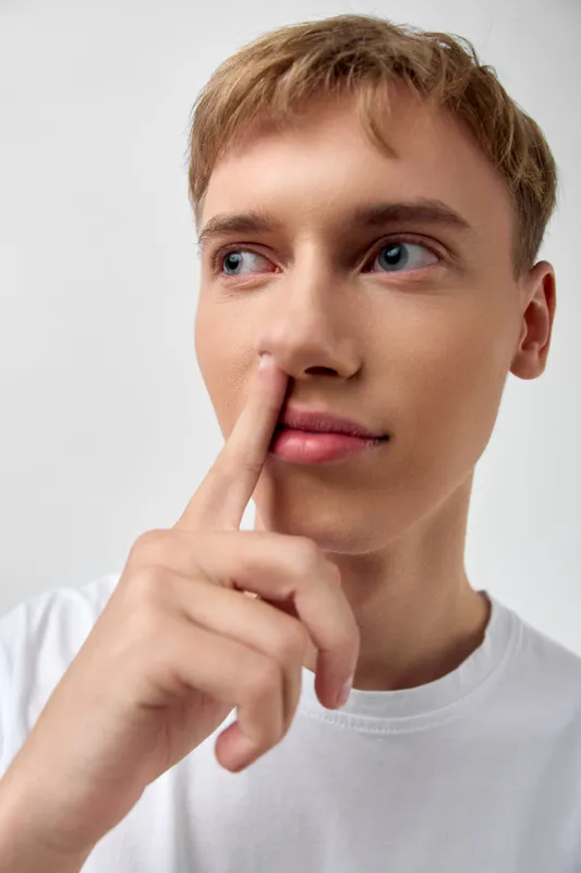Man with finger to lips signaling quiet and contemplation, a thoughtful gesture conveying secrecy, focus, and a moment of reflection in a studio setting with soft lighting and a clean background