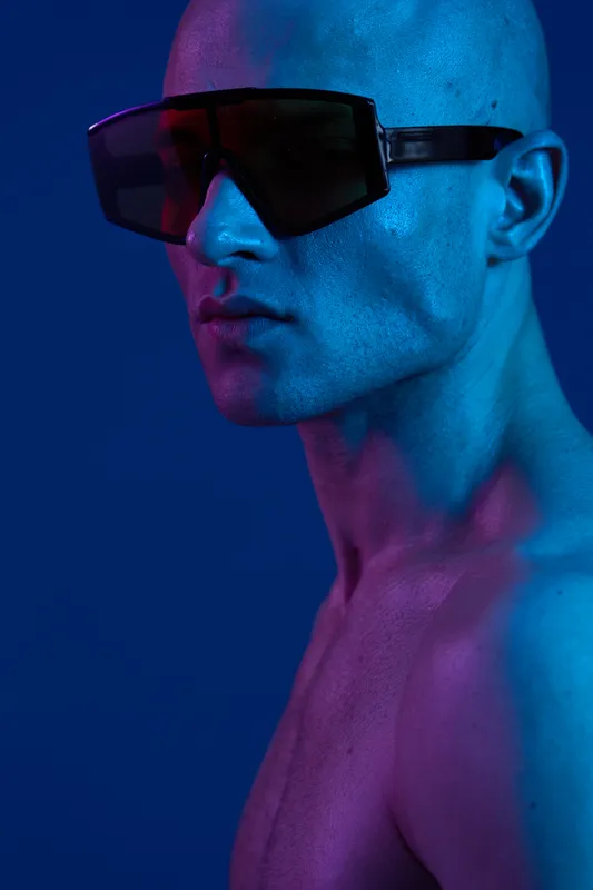 Stylish man with futuristic sunglasses showcasing vibrant colors and strong lighting, emphasizing bold personality in a striking setting.