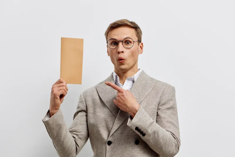 surprised young caucasian man wear glasses beige jacket hold paper show finger isolated on white background digital detox concept with smartphone detached