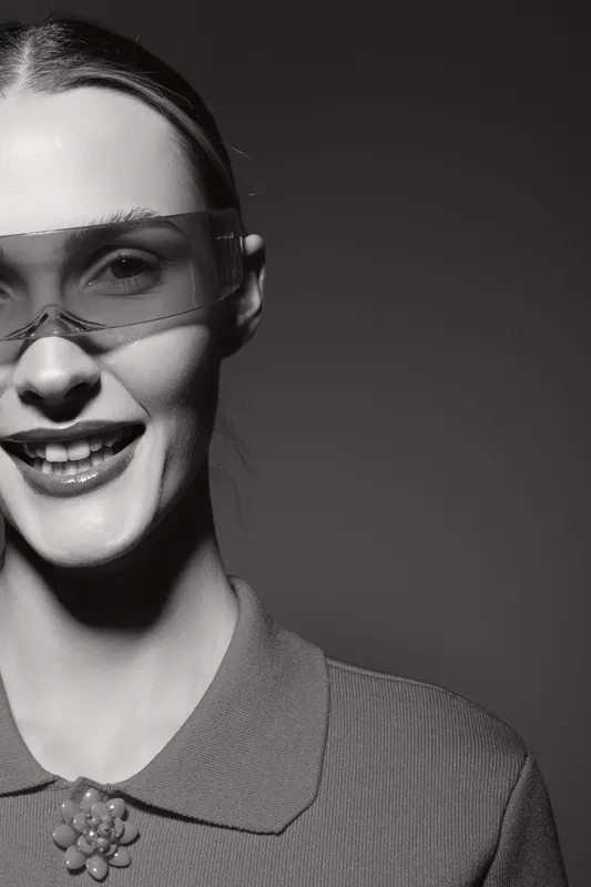 Close-up of a smiling young white woman wearing transparent glasses and a collared top, studio portrait in black and white with modern style.