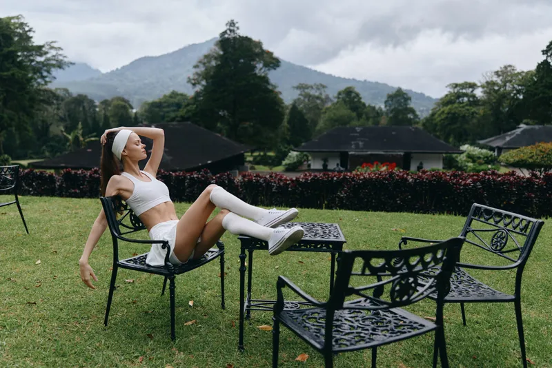 Stylish model in sporty outfit relaxing outdoors, embodying serenity and confidence in natural scenery with mountains and greenery