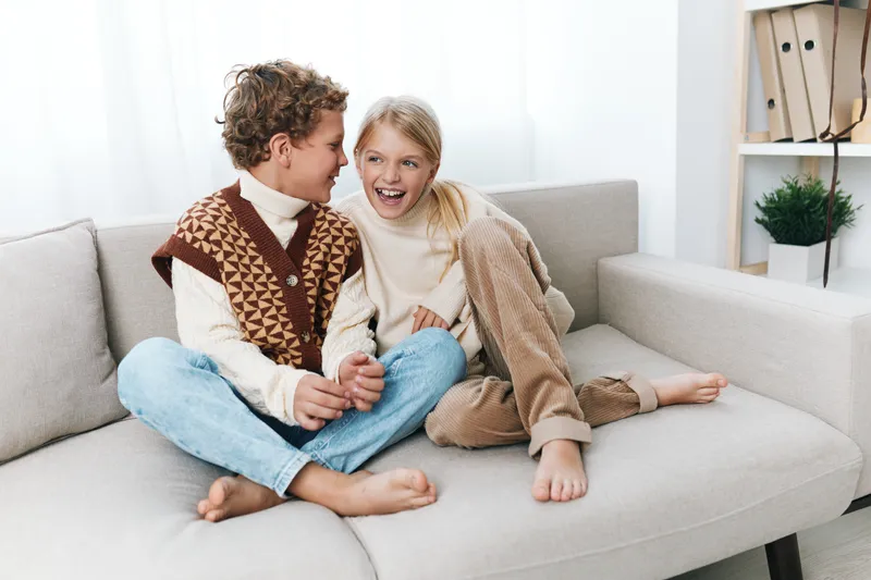 Authentic scene of children enjoying playful moments at home, showcasing school themed lifestyle and cozy fashion as they laugh together on a sofa, creating relatable, heartwarming moments.