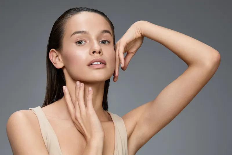 Young woman with natural beauty posing gracefully, showcasing healthy skin and a serene expression against a neutral gray background
