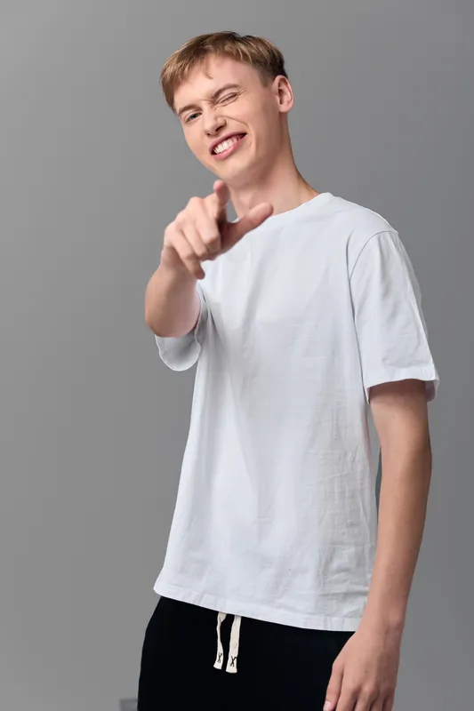Young man with a pointing gesture in casual attire and white t shirt against a neutral studio backdrop, conveying confidence and direct communication
