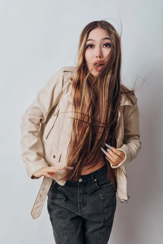 Young woman with long hair and beige jacket posing with expressive face on plain background for fashion, style, beauty and modern casual look indoors.