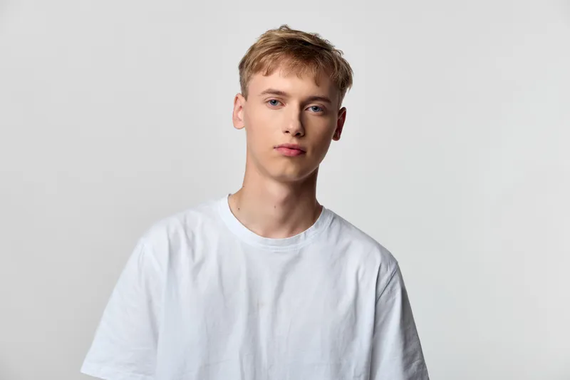 Young man wearing a white shirt in a studio with a neutral background, relaxed pose and calm expression, ideal for fashion, lifestyle or model photography concepts for campaigns