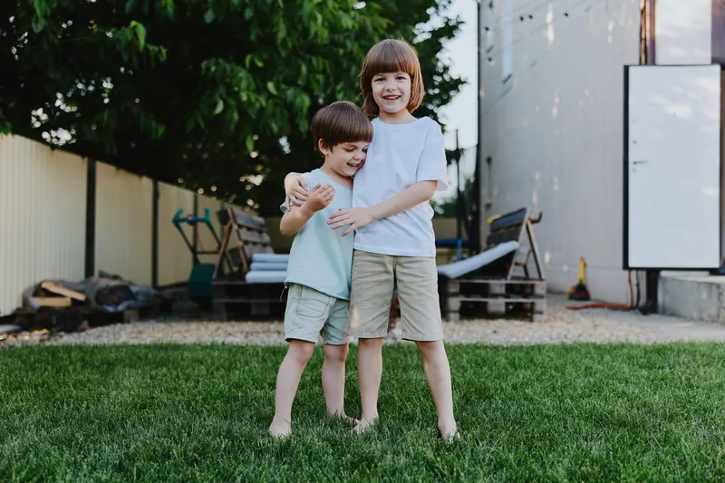 Two happy boys playing together outside in a grassy area, showcasing friendship and joy. Their casual summer outfits reflect a cheerful atmosphere and carefree spirit.