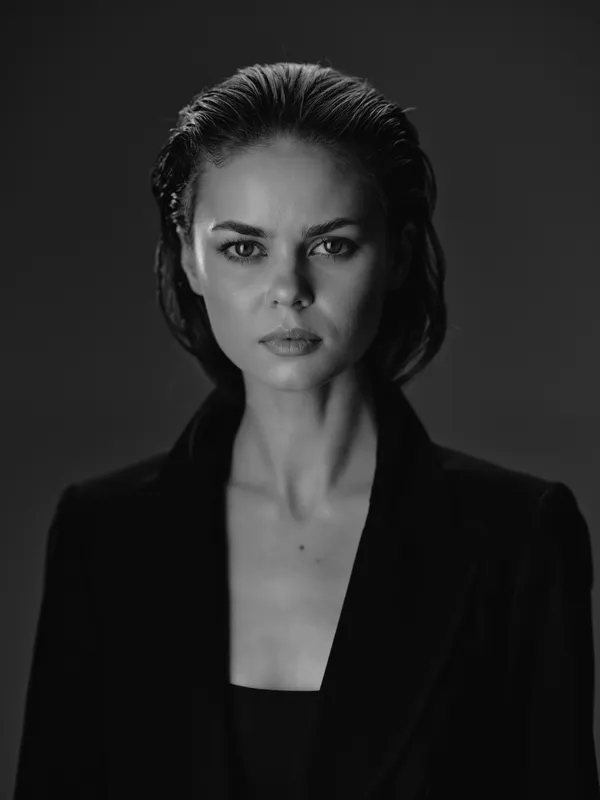 Black and white portrait of a serious woman with wet hair wearing a dark jacket in a studio setting
