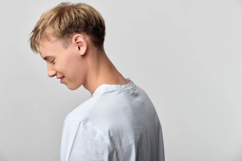 Profile of a young man in a white shirt, captured in a calm, thoughtful moment from the side, studio setting with a clean neutral background and minimal, serene mood.