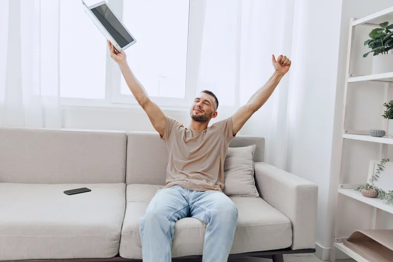 Happy man celebrating digital detox at home with a tablet, embracing emotional minimalism and solo living as a choice for better mental health.