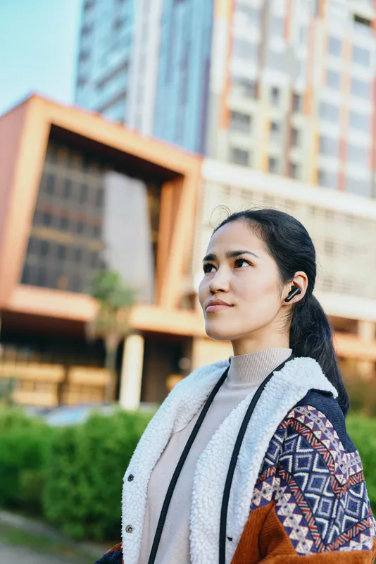 Woman in a patterned jacket stands outdoors among modern urban architecture, looking upward with a calm gaze, daylight glow, and confident fashion sense, capturing a contemporary cityscape,