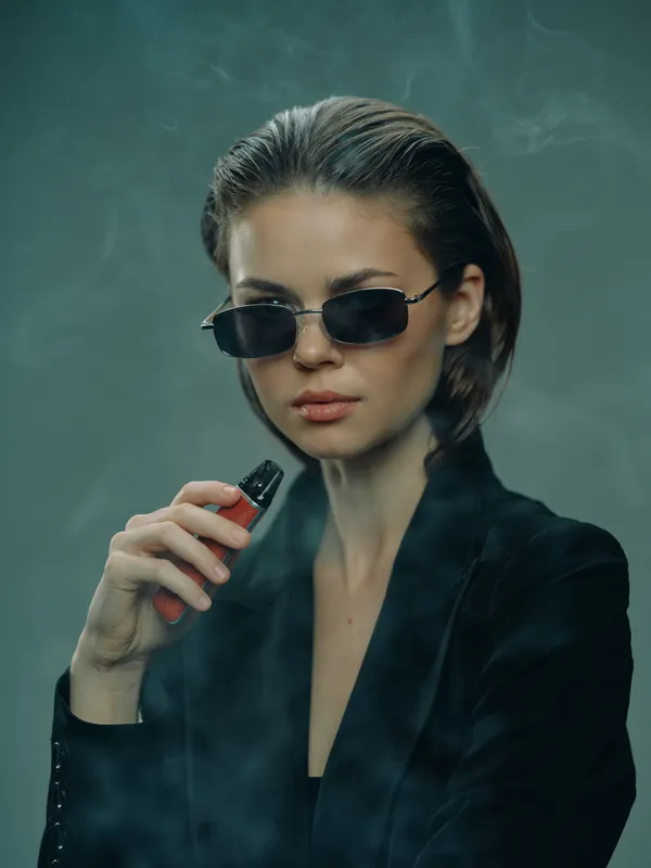 Stylish woman with sunglasses vaping in smoky atmosphere, wearing dark blazer, confident and modern
