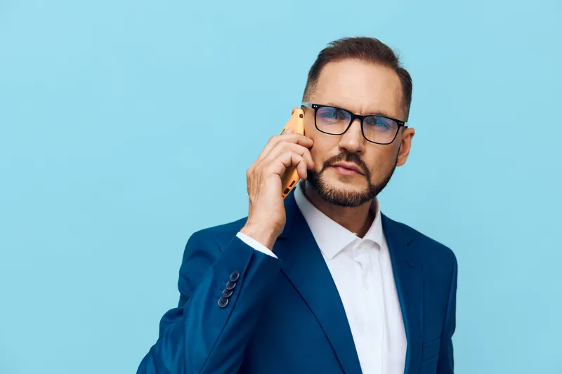 A business professional man speaks on a mobile phone against a solid colored background, conveying focus, confidence, and concentration in a corporate setting.