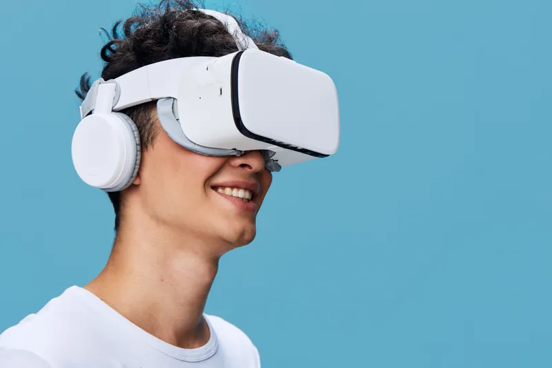 young man enjoying virtual reality headset with headphones, smiling and immersed in blue background, casual white shirt, technology concept