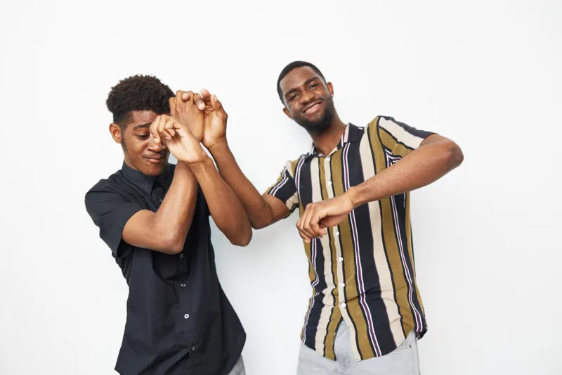 Two joyful African American men expressing happiness with playful gestures, celebrating friendship and connection in a vibrant atmosphere.