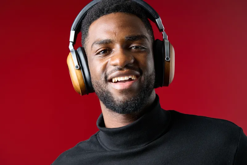 Smiling young African man wearing stylish headphones against a vibrant red background, representing music enjoyment and modern lifestyle
