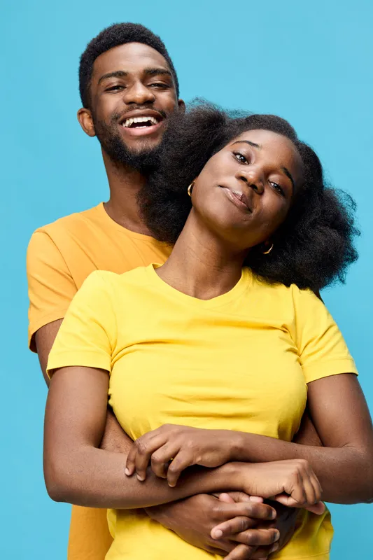 Young African couple in bright yellow and orange t shirts, smiling happily against a vibrant blue background A joyful representation of love and connection