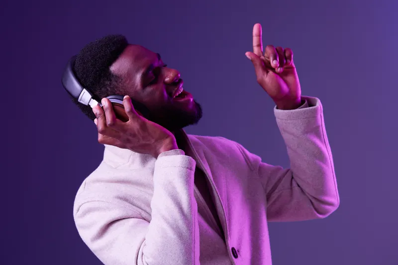 Stylish African man enjoying music with headphones in a vibrant purple background, expressing joy and passion through song