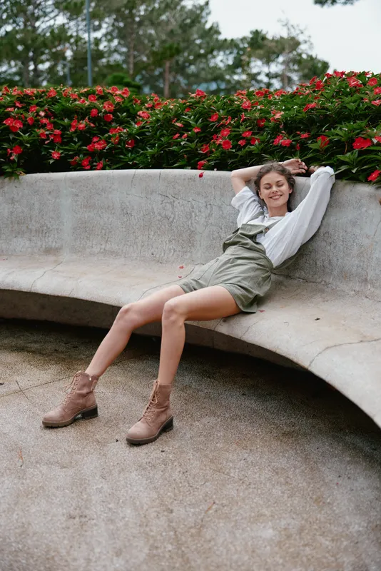 Cheerful young woman in trendy overalls and boots, enjoying a spring day among vibrant flowers, conveying joy and relaxation in a casual outdoor setting