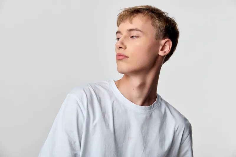 Young man, white shirt, studio setting, calm pose with sideways gaze, minimal fashion vibe, clean aesthetic for stock photography, suitable for lifestyle, editorial or branding projects