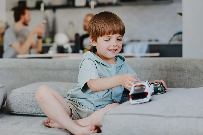 Happy boy playing with toy cars in a cozy living room, surrounded by family. Bright and engaging atmosphere enhances the playful mood of childhood.