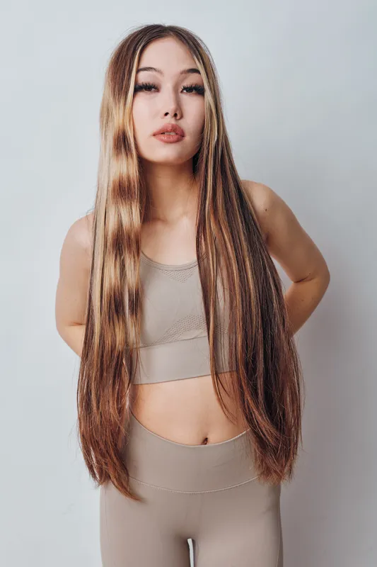 Young woman with long straight hair wearing beige sportswear posing against white background, beauty and fitness concept for healthy lifestyle and fashion model portrait.