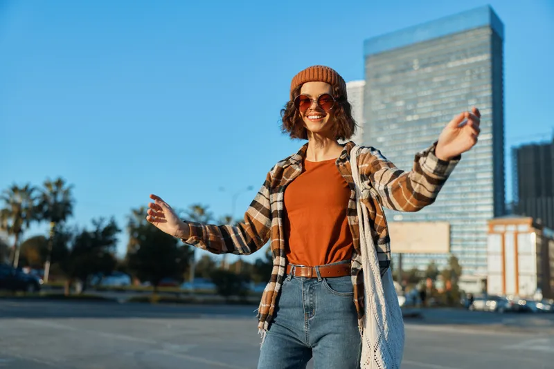 Woman smile urban candid lifestyle authenticity captured in golden hour glow, joyful young person in beanie and sunglasses with tote bag, emotional storytelling and mindful living vibe