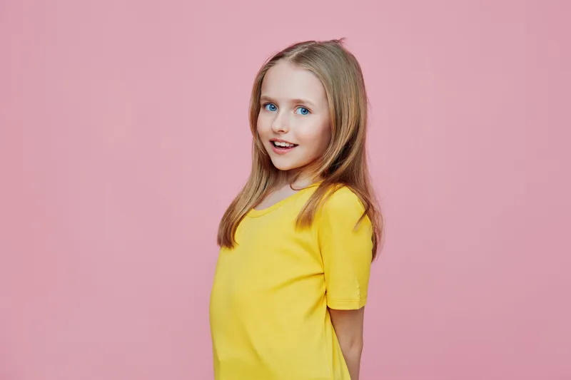Happy girl in a yellow shirt with long hair smiles against a pink background, embodying joy and innocence, perfect for children s concepts and marketing