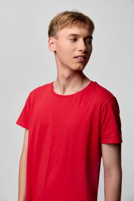 Red shirt clad young man in casual fashion stands in a studio with soft lighting, showing a profile pose and confident expression, perfect for fashion, lifestyle, or product styling, clean background