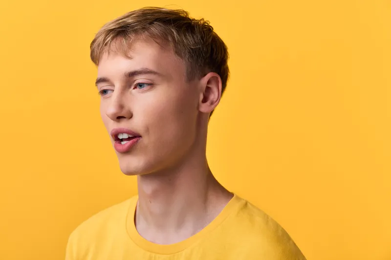 Young man in a yellow shirt speaks against a vivid yellow backdrop in a casual studio setting, capturing expressive speech, closeup mood and clear communication