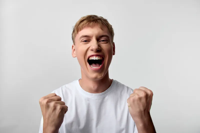 Excited, celebration, enthusiasm, shouting, fists, energy, a man in a white tee shows cheer and strong fists, conveying motivation and victory for campaigns