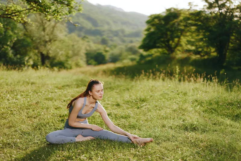 Serene young woman practicing yoga outdoors in a lush green field, embodying wellness and mindfulness in a tranquil natural setting