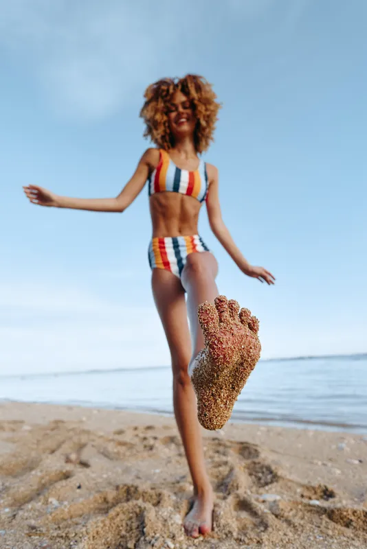 Woman on beach in summer wearing swimsuit, curly hair jump, happiness and freedom in the scene, ocean waves behind, colorful swimwear, natural sunlight, wellness