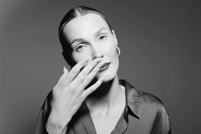 Caucasian woman with fair skin touches face with hand in black and white studio portrait, elegant mood and soft lighting.